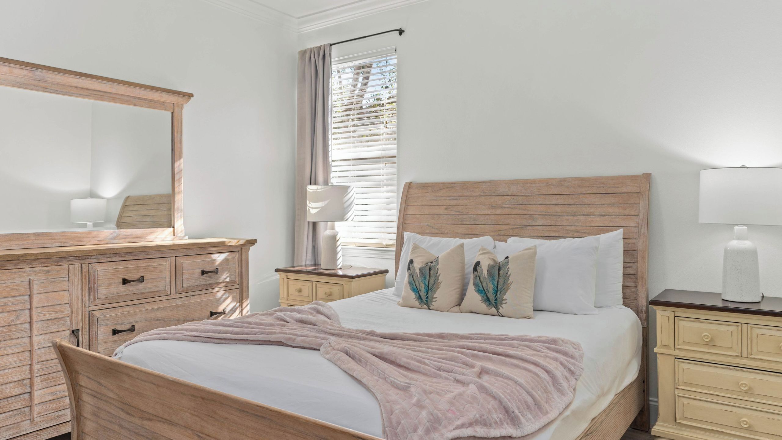 A bedroom with a wooden bed, a dresser, a nightstand, and a window with blinds.