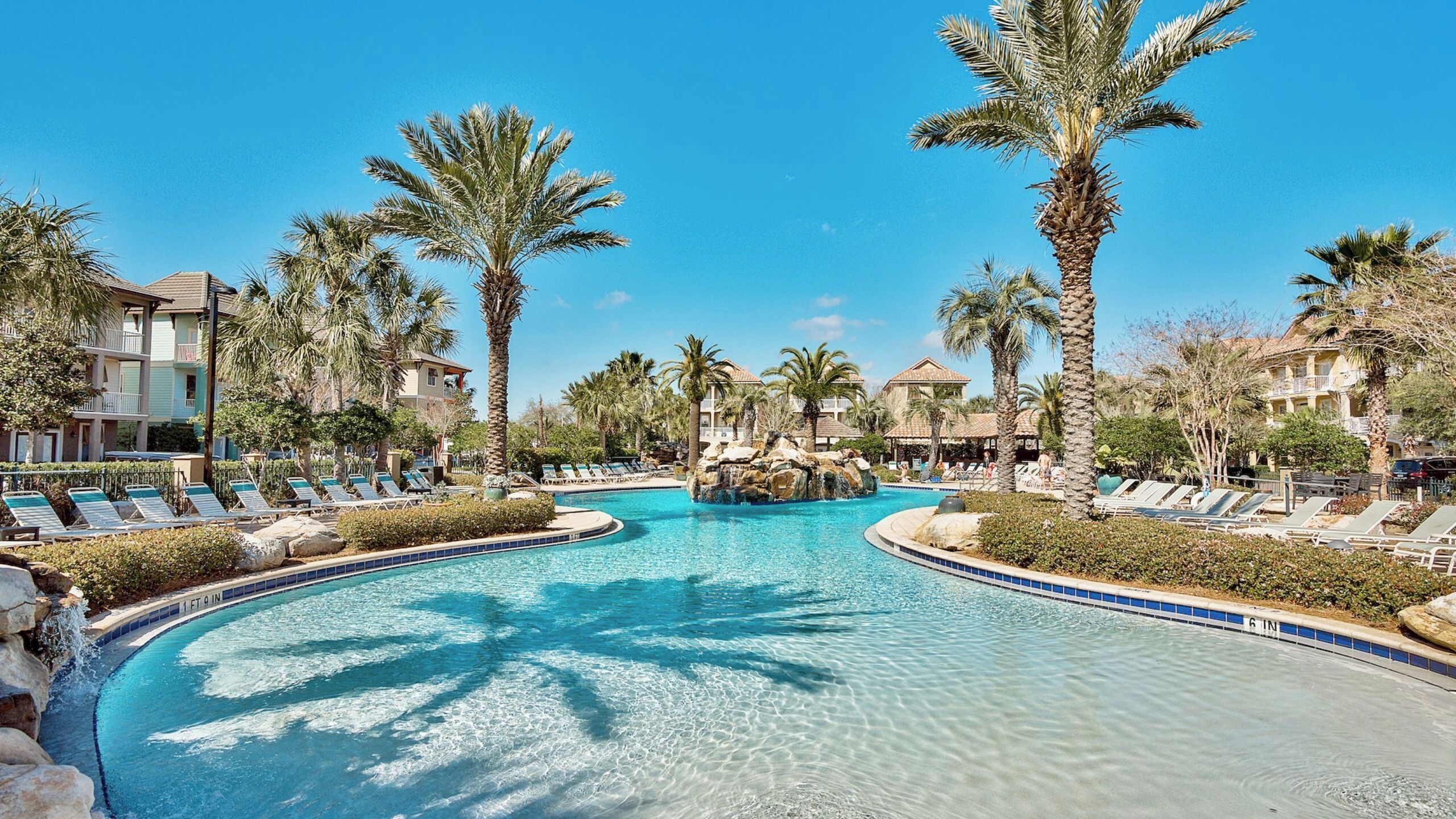 A resort pool with palm trees, lounge chairs, and a clear blue sky.
