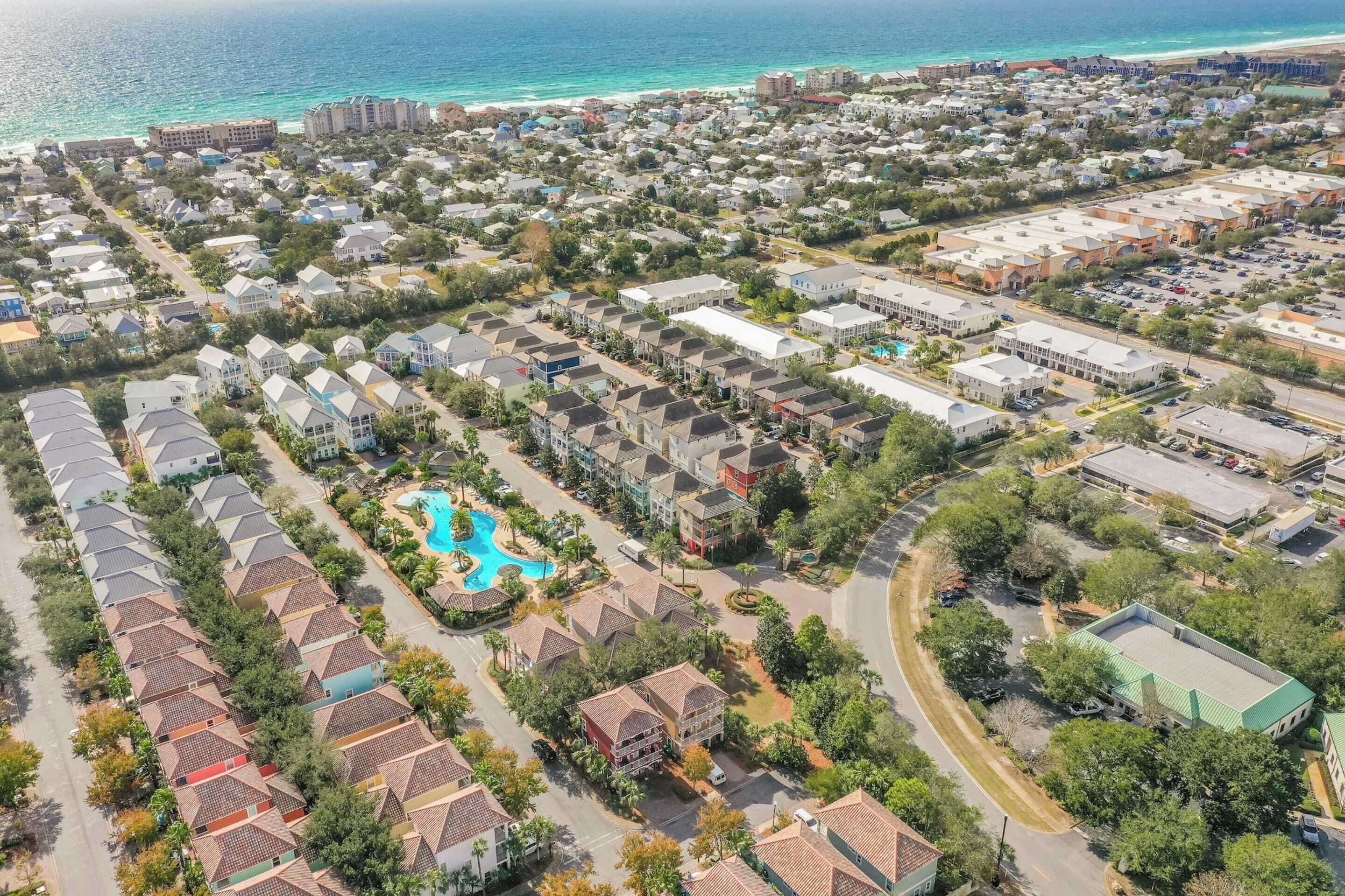 Vue aérienne d’un quartier résidentiel avec des maisons, une piscine et une plage en arrière-plan.