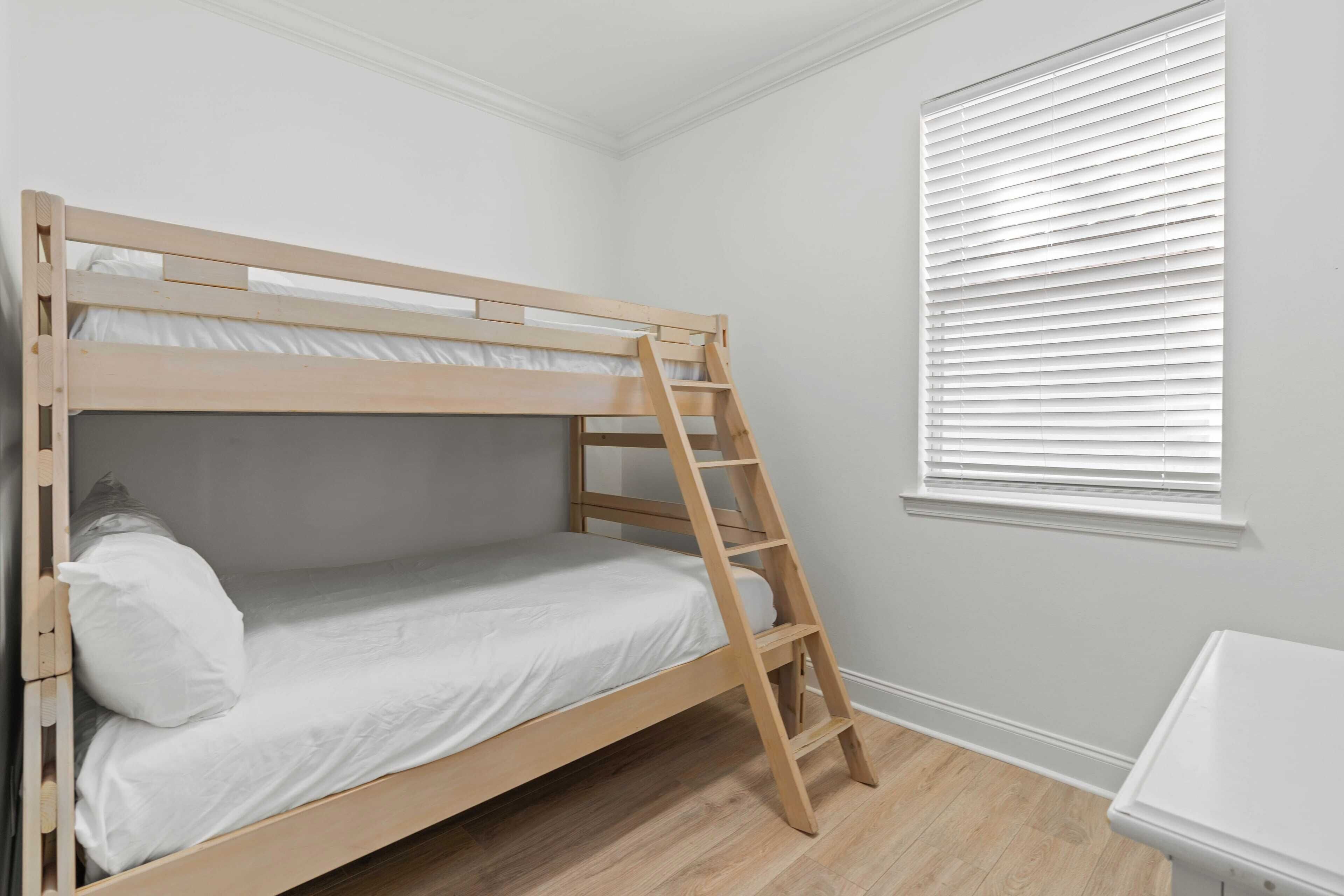 Una litera con escalera de madera, ropa de cama blanca y una ventana con persianas.