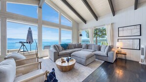 A spacious living room with a large sectional sofa, a round coffee table, and a view of the sea.