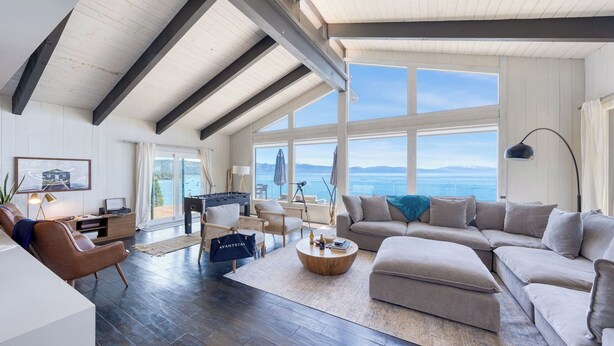A spacious living room with a high ceiling, large windows offering a view of the sea, a cozy seating area, and a foosball table.