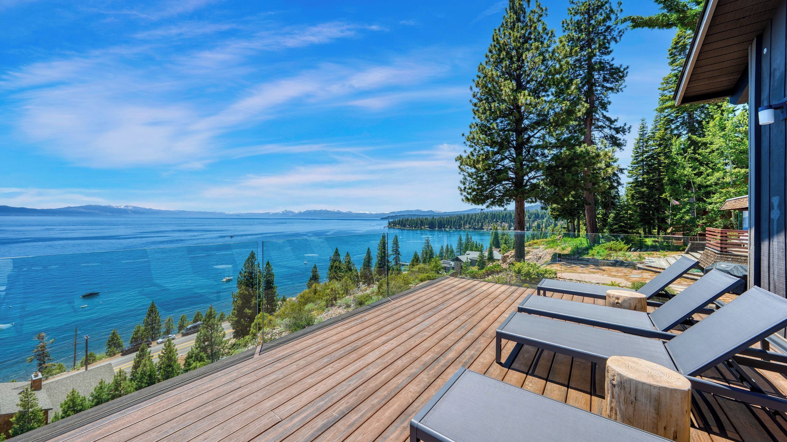 A wooden deck with lounge chairs overlooking a lake with a clear view of mountains in the distance.