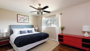 A bedroom with a bed, a ceiling fan, a window with curtains, a red cabinet, and a wall art piece. - West Ridge by Avantstay Pool, Fire Pit, Al Fresco Dining 7 Mins to Downtown (Scottsdale)