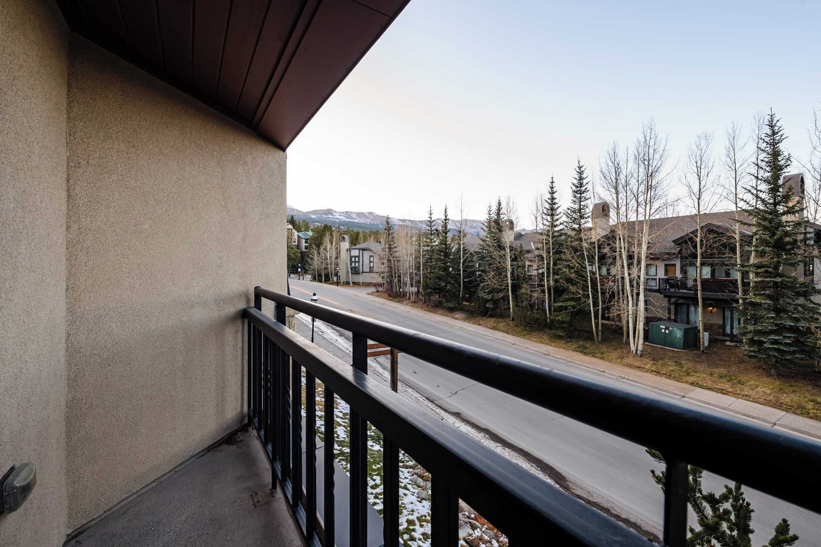 Ein Balkon mit Blick auf eine Straße und Bäume, ein Gebäude im Hintergrund und ein Gebirge.