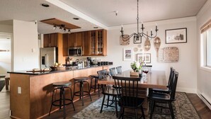 Une cuisine moderne avec des meubles en bois, un îlot central, des tabourets de bar et une table à manger avec des chaises.