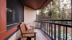 Un banc en bois avec un coussin à rayures, placé sur un balcon doté d’une rambarde noire, d’où l’on peut admirer une zone boisée.
