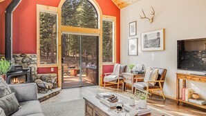 Uma sala de estar aconchegante com lareira, assentos confortáveis e grandes janelas com vista para a floresta.