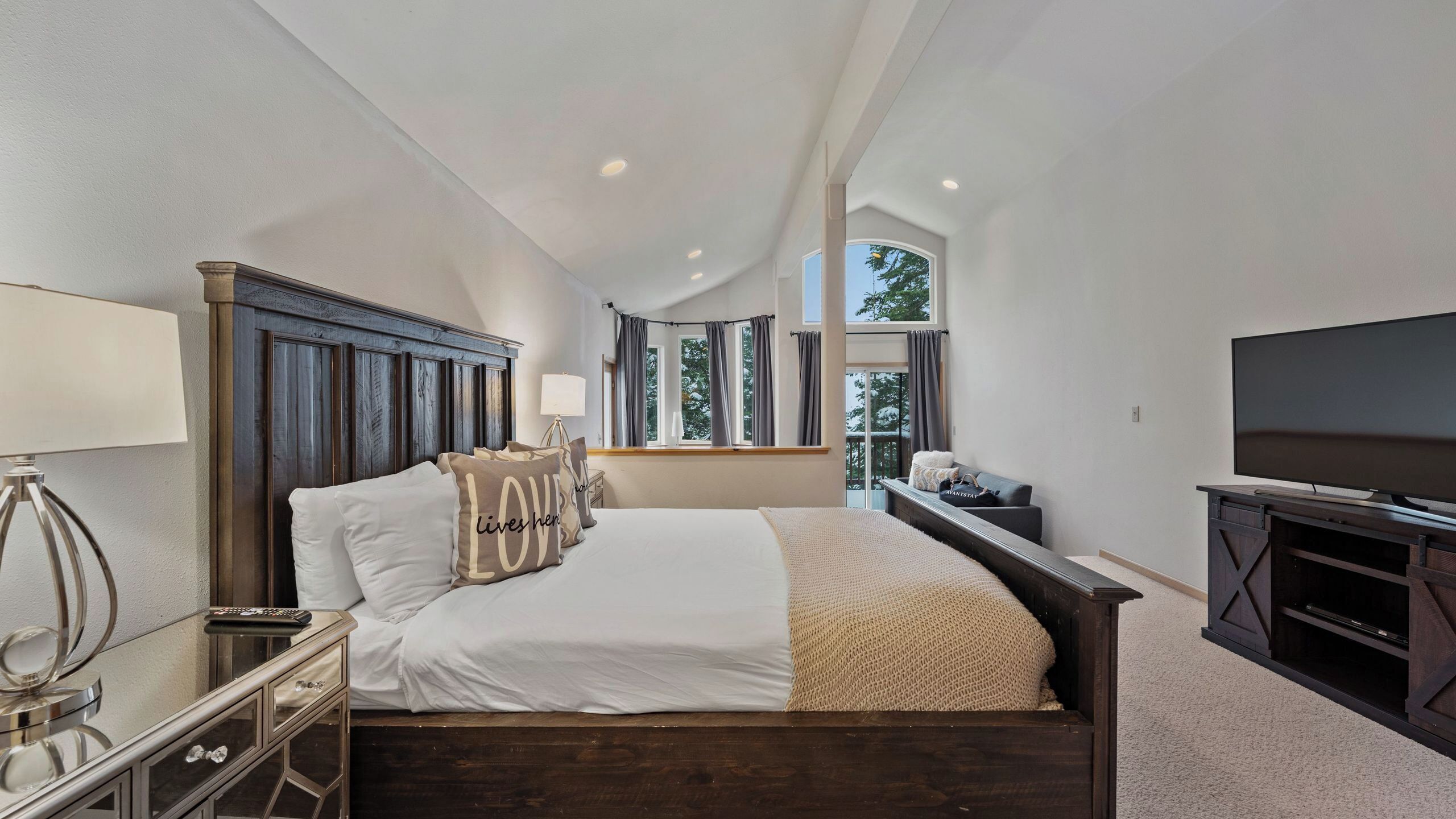 A bedroom with a large bed, a TV, a dresser, and a window with curtains.