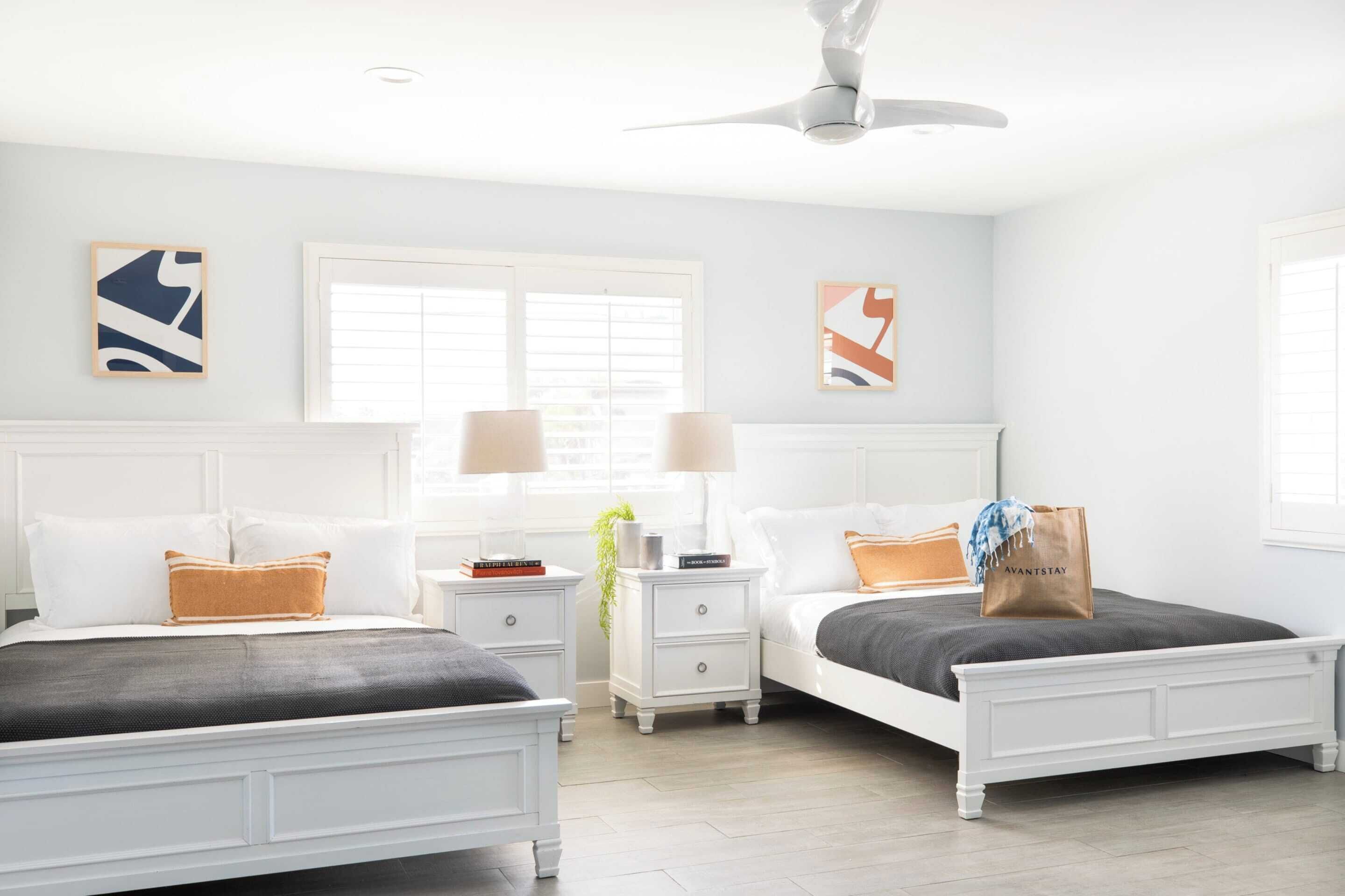 A bedroom with two beds, white nightstands, and a ceiling fan.