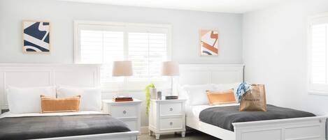A bedroom with two beds, white nightstands, and a ceiling fan.