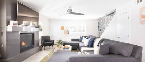 A modern living room with a fireplace, grey sofa, and a staircase.