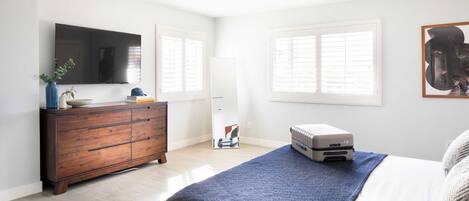A bedroom with a bed, a dresser, a ceiling fan, a radiator, and a TV on the wall.