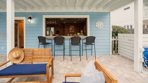 A covered patio with a bar area, wooden furniture, and a blue wall. - Blue Jay By Avantstay Spectacular Destin Oasis w/ Pool Walking Distance to Beach (Destin)