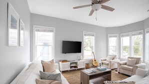 A spacious living room with a white sofa, a coffee table, and two armchairs. A flat-screen TV is mounted on the wall, and there is a guitar leaning against the wall. - Blue Jay By Avantstay Spectacular Destin Oasis w/ Pool Walking Distance to Beach (Destin)