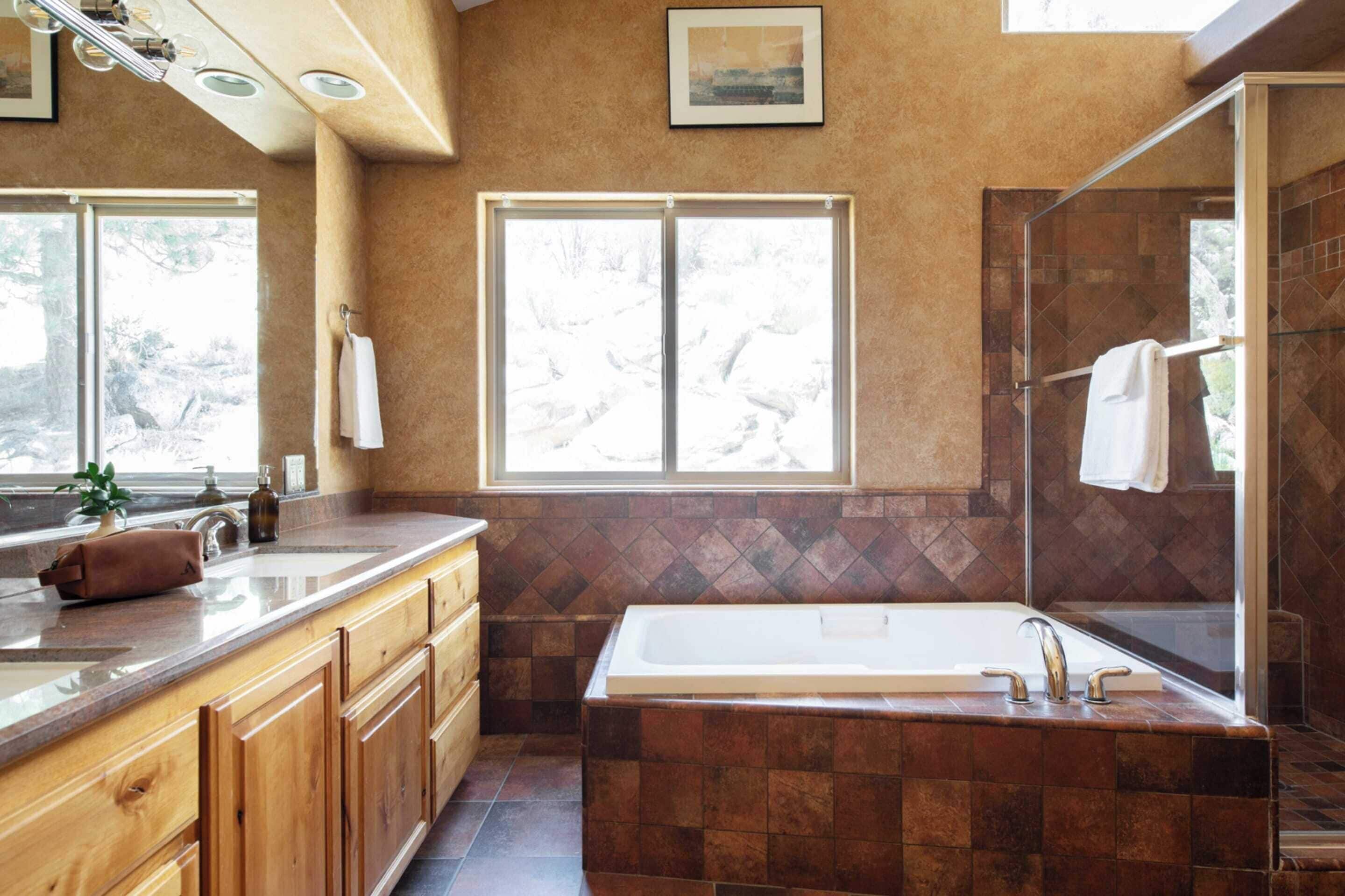 Un baño moderno con una bañera grande, armarios de madera, un lavabo y una ducha con mampara de vidrio.