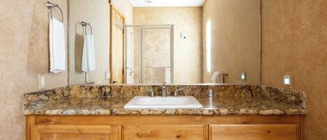 Un baño con lavamanos de encimera de granito, armarios de madera y un espejo grande.