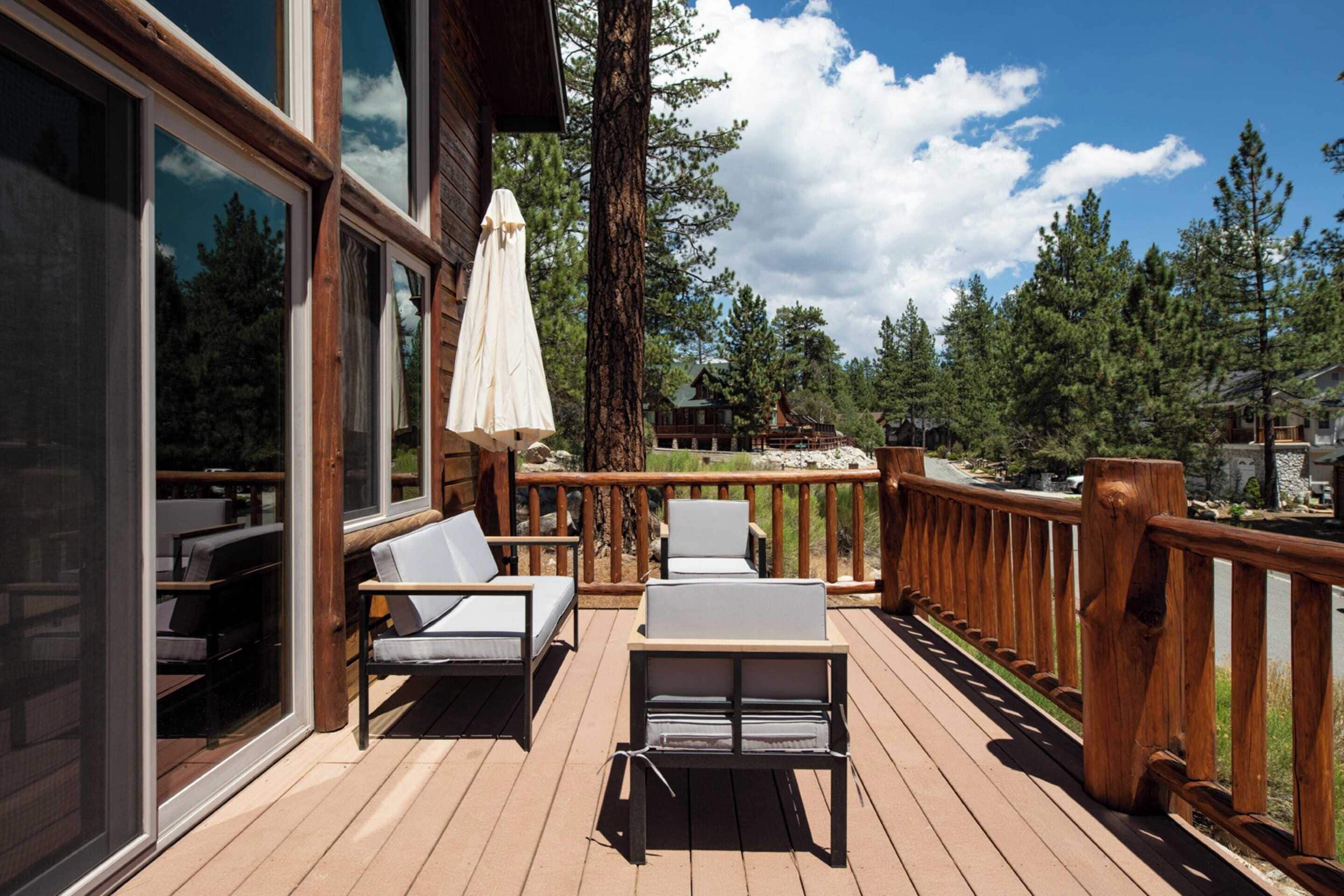 A wooden deck with outdoor seating and a view of a forest.