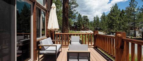 A wooden deck with outdoor seating and a view of a forest.