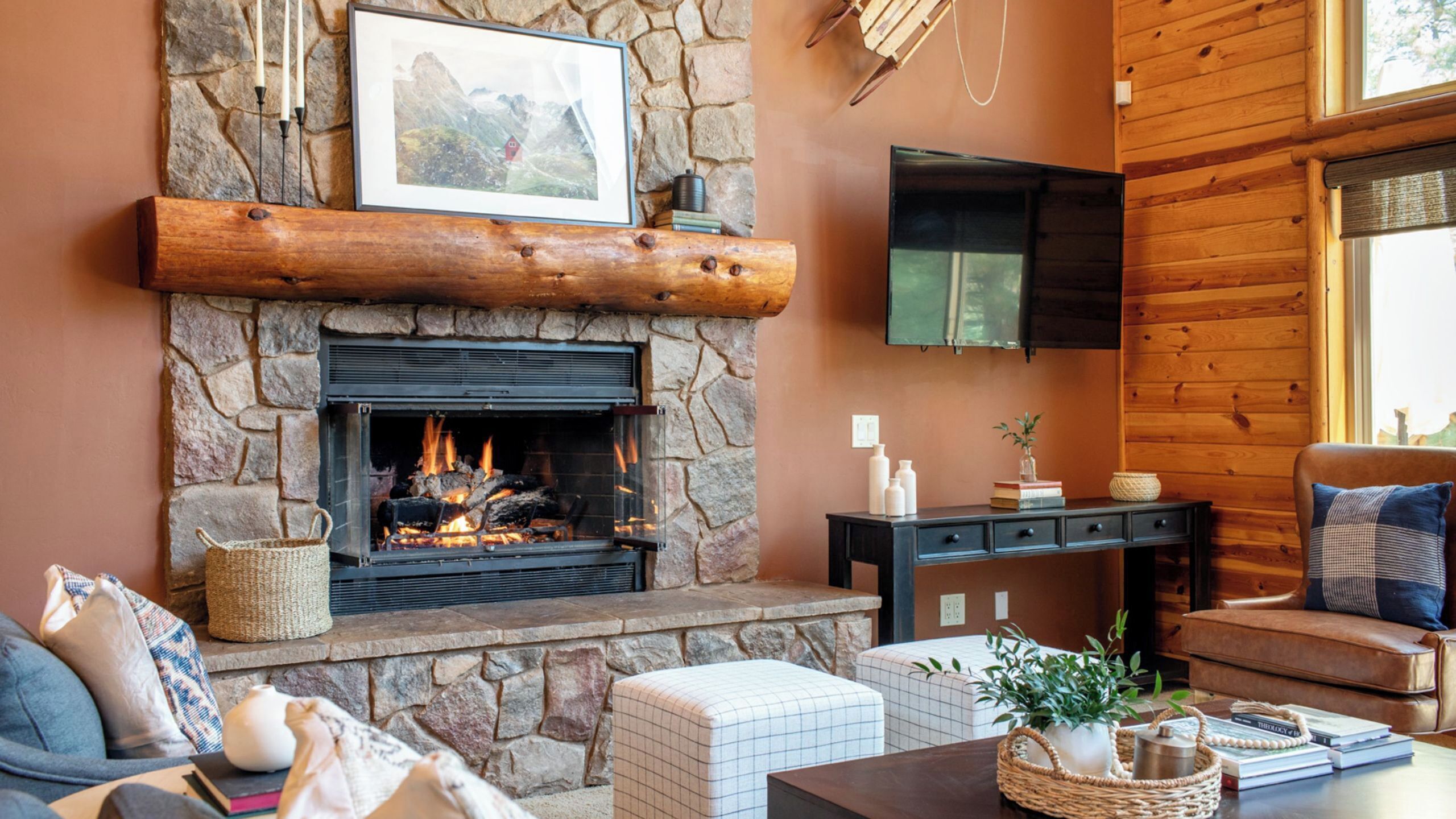 A stone fireplace with a log fire, a mounted television, and a cozy seating area with cushions and a coffee table.