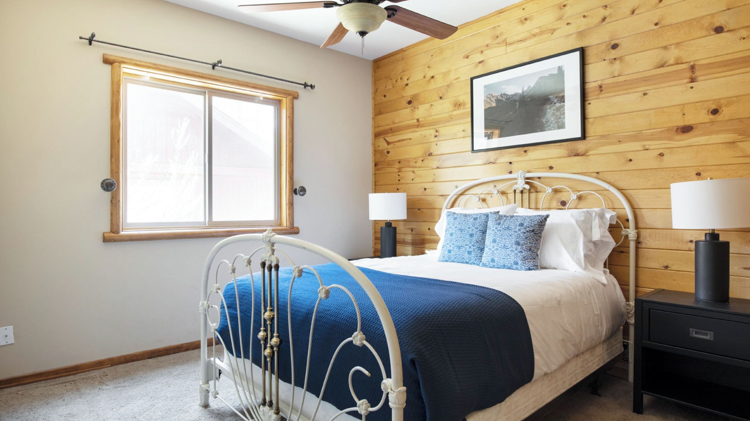 Een slaapkamer met een bed, twee nachtkastjes, een raam, een plafondventilator en een houten wand.