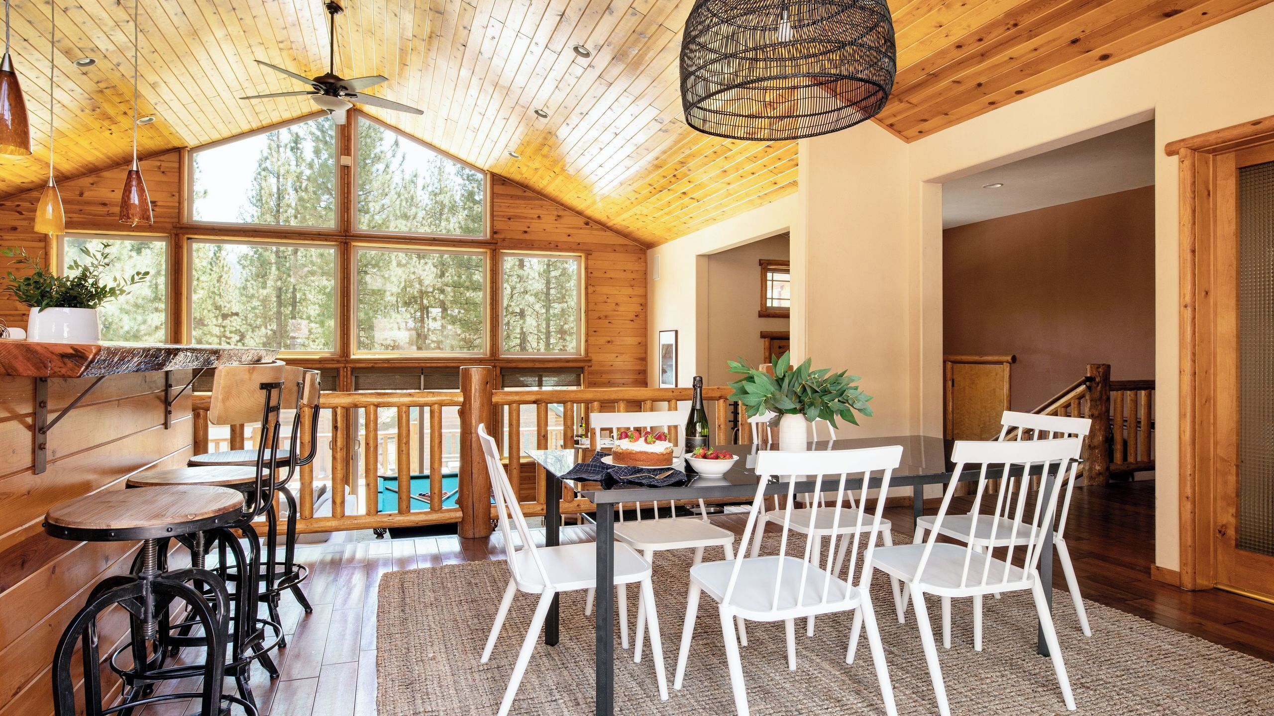 Un intérieur en bois comprenant un coin repas, un ventilateur de plafond et de grandes fenêtres.