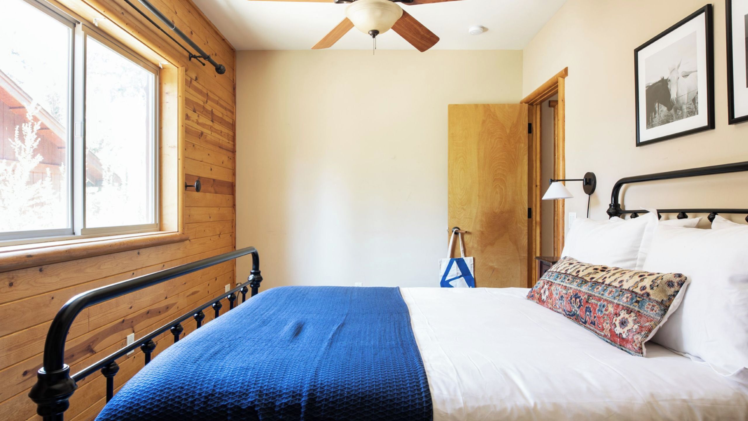 Quarto com cabeceira de madeira, cama com manta azul, travesseiro branco e ventilador de teto.
