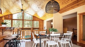 A wooden interior with a dining area, a ceiling fan, and large windows. - Bernard by Avantstay Luxurious Cabin in Big Bear w/ Hot Tub & Pool Table (Big Bear Lake)