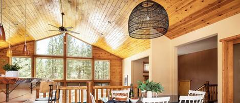 A wooden interior with a dining area, a ceiling fan, and large windows.