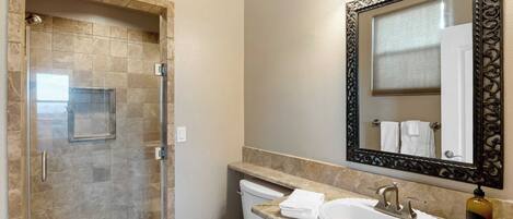 A bathroom with a glass-enclosed shower, a white toilet, a sink with a marble countertop, and a large mirror with an ornate frame.
