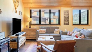 Un salon chaleureux avec un plafond en bois, un canapé, une table basse et un téléviseur.