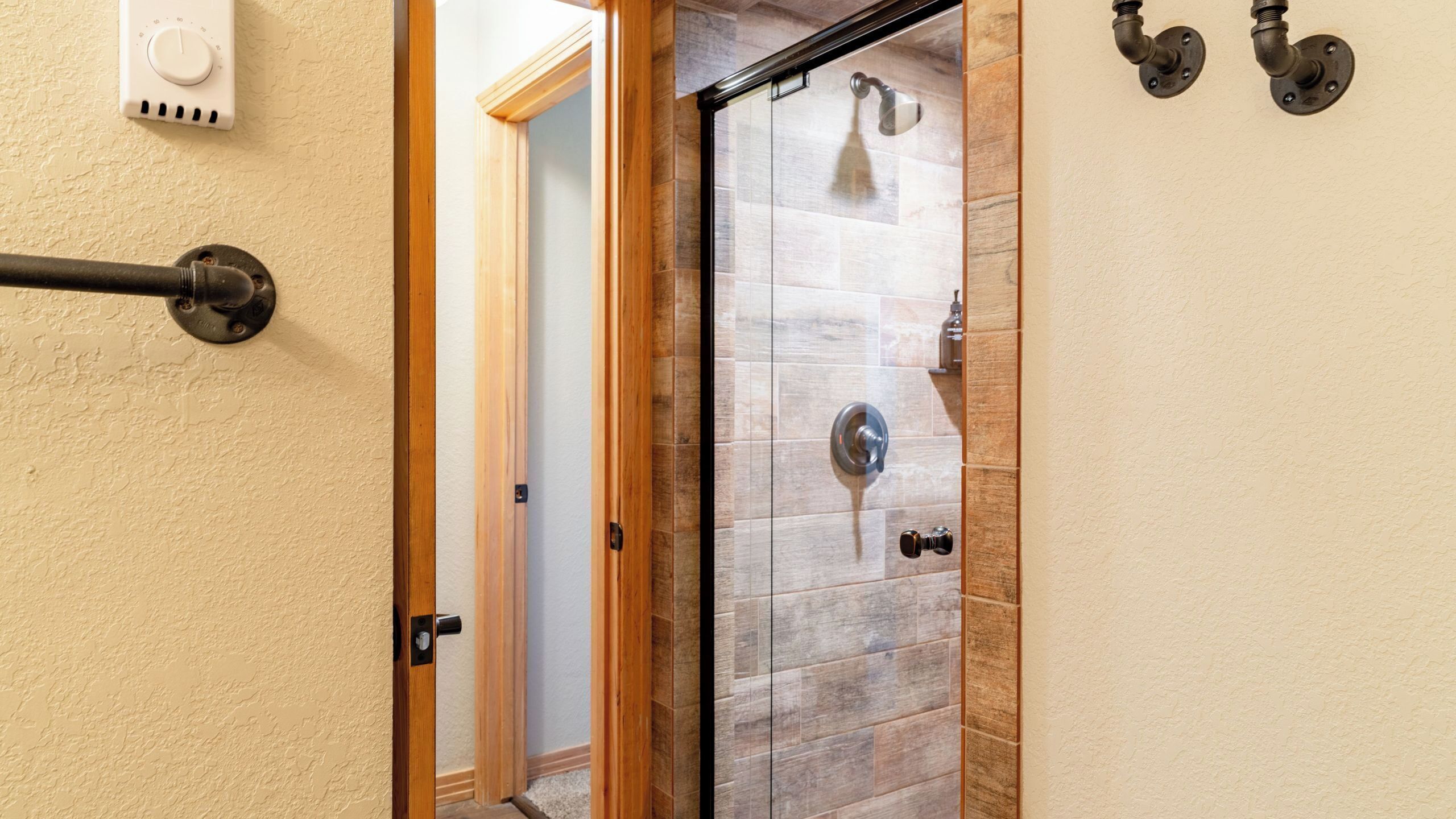 Une salle de bain avec une porte de douche en verre, un thermostat et un porte-serviettes.