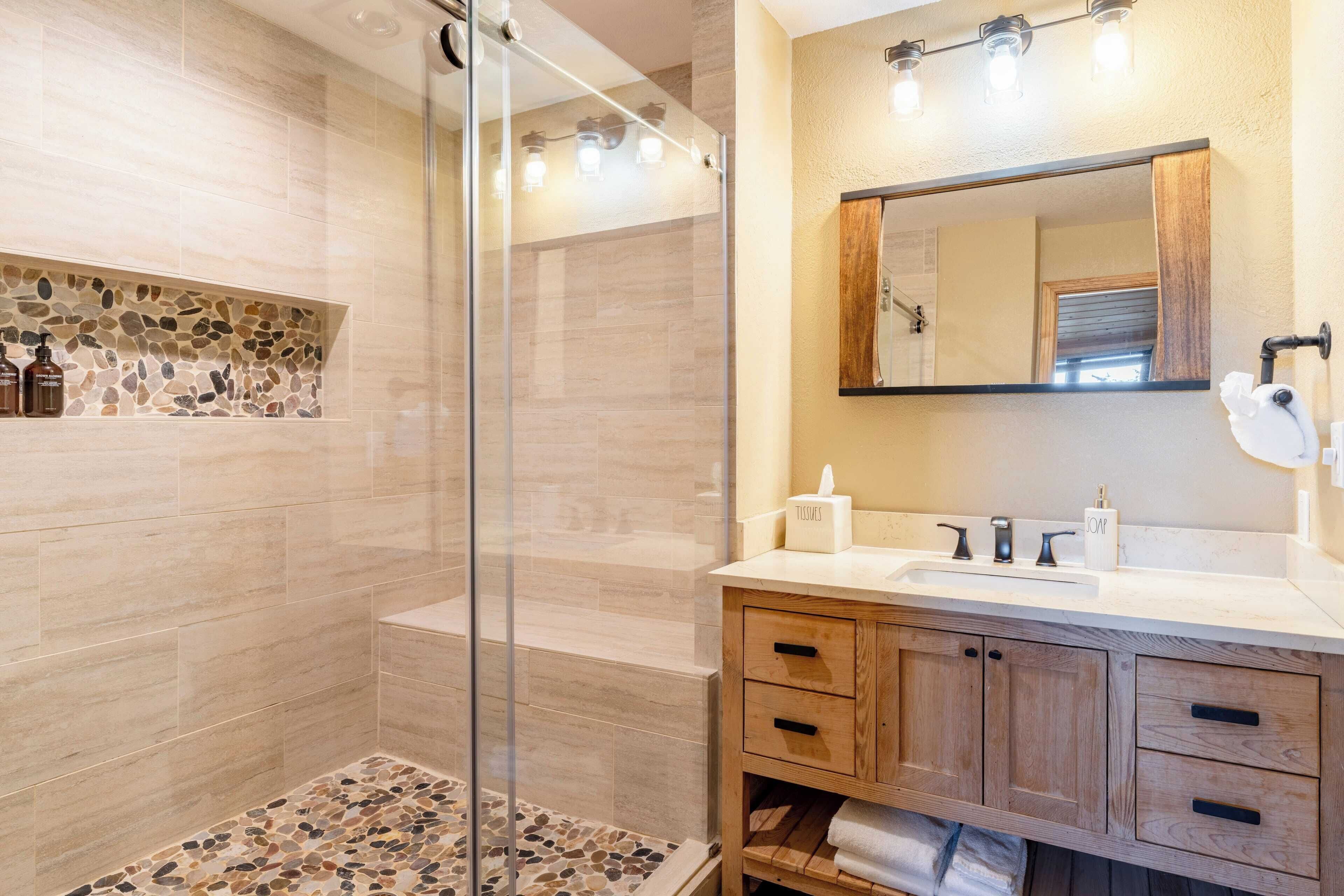 A modern bathroom with a glass shower enclosure, a wooden vanity with a sink, and a mirror above.