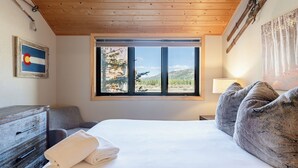 Une chambre avec une grande fenêtre, un lit, une commode et une lampe.