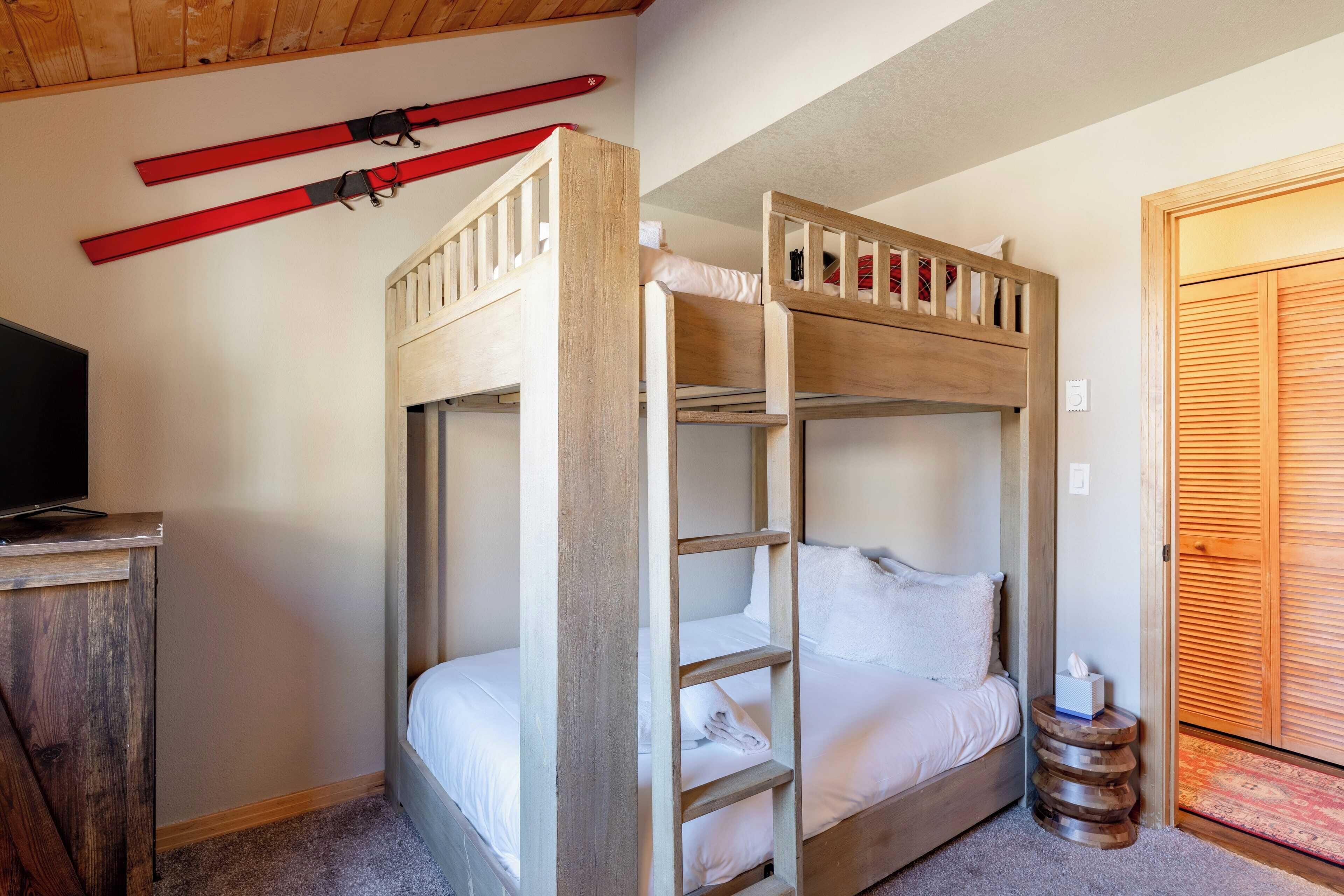 A bunk bed room with a wooden ladder, a small table with a tissue box, and a TV on a wooden cabinet.