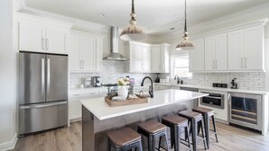 A modern kitchen with white cabinets, stainless steel appliances, and a central island with stools. - Fin by Avantstay 9 BR Destin Oasis With Pool & Spa Walk to Beach (Panama City Beach)