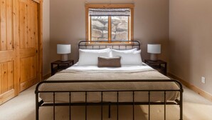 Une chambre à coucher avec un lit, deux tables de chevet, une fenêtre donnant sur des rochers et une porte en bois.