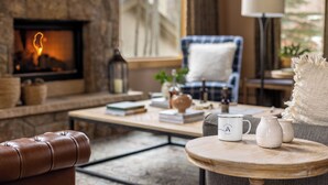 Un salon chaleureux avec une cheminée, un fauteuil bleu, une table basse ronde agrémentée d’objets décoratifs et un canapé en cuir.