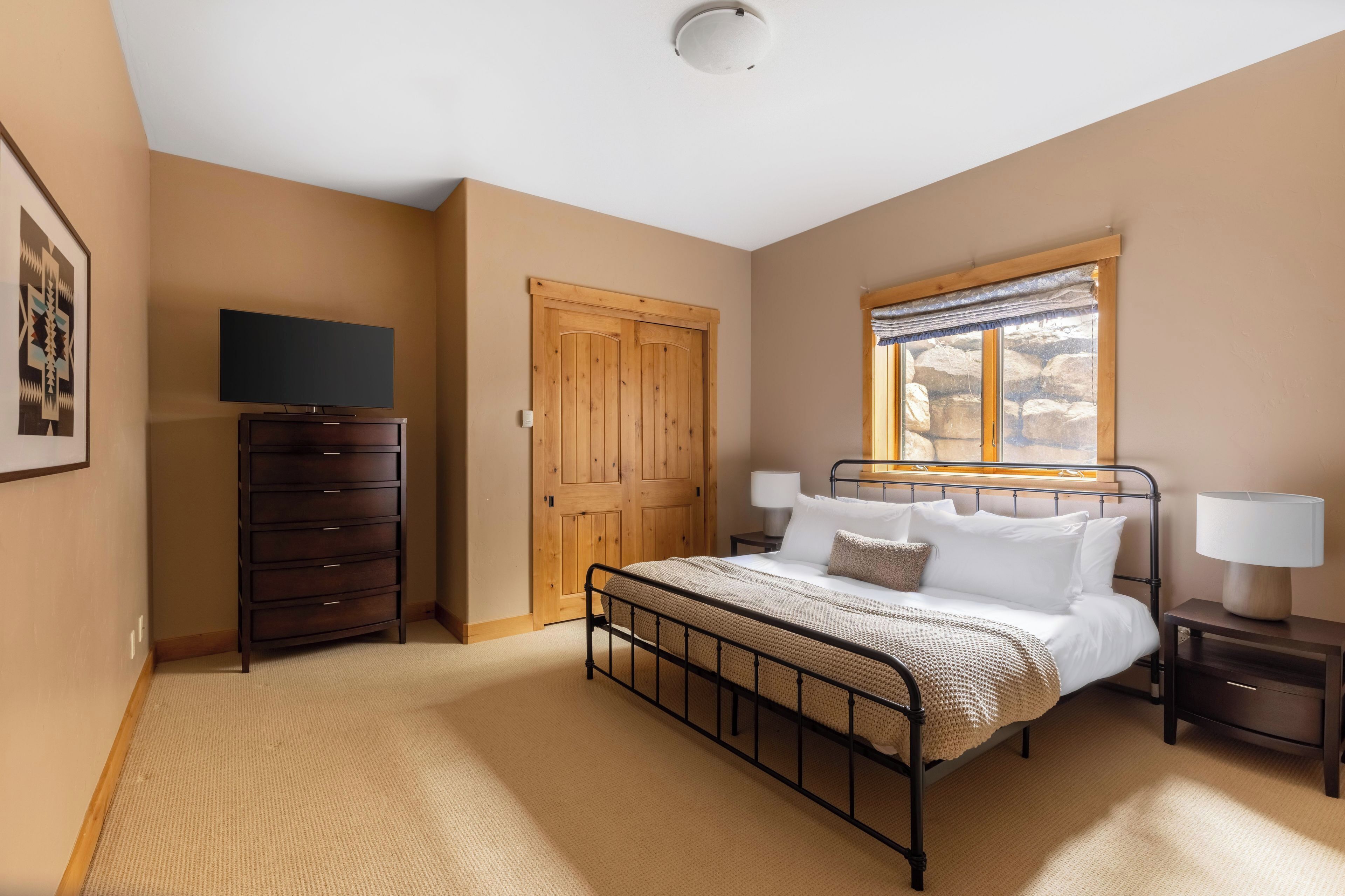 A bedroom with a bed, wooden wardrobe, bedside tables, a television, and a window with a view.