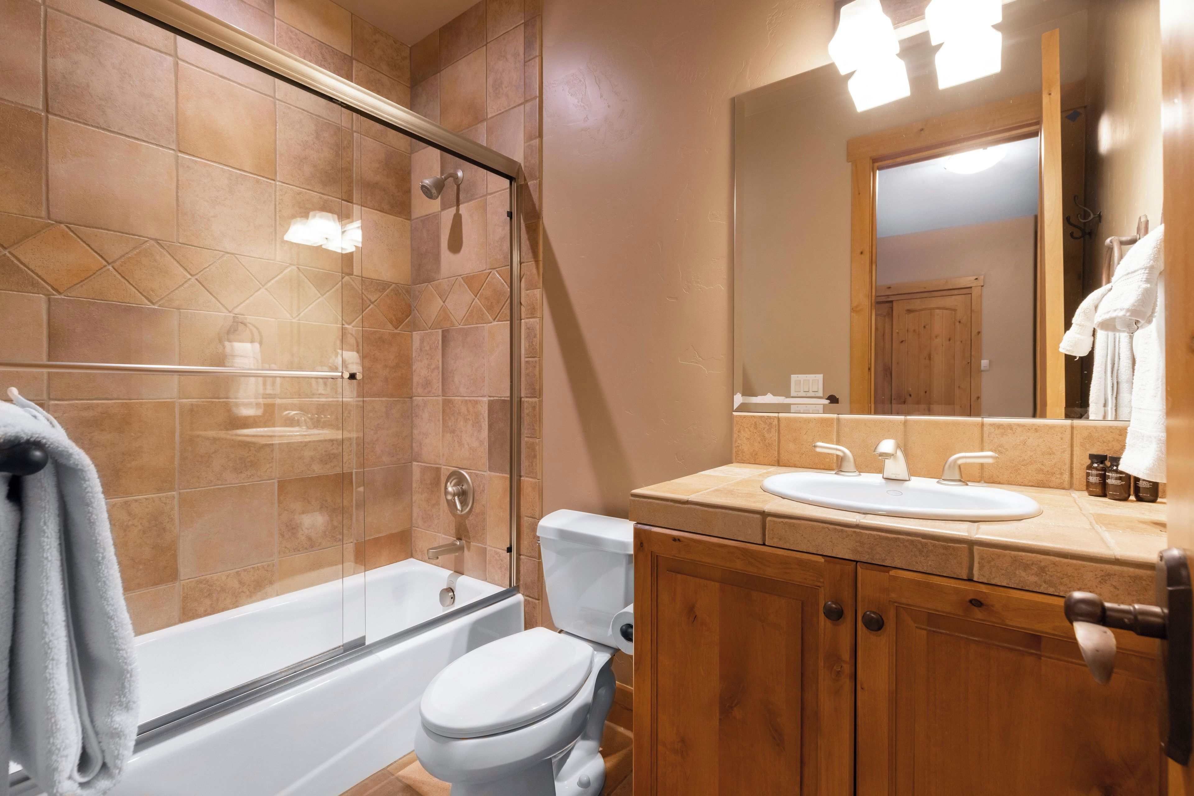 A bathroom with a glass-enclosed shower, a white toilet, a wooden vanity with a sink, and a mirror.