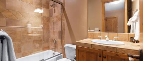 A bathroom with a glass-enclosed shower, a white toilet, a wooden vanity with a sink, and a mirror.