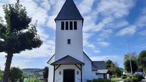 Une église blanche avec un clocher en flèche, une porte noire et une petite fenêtre.