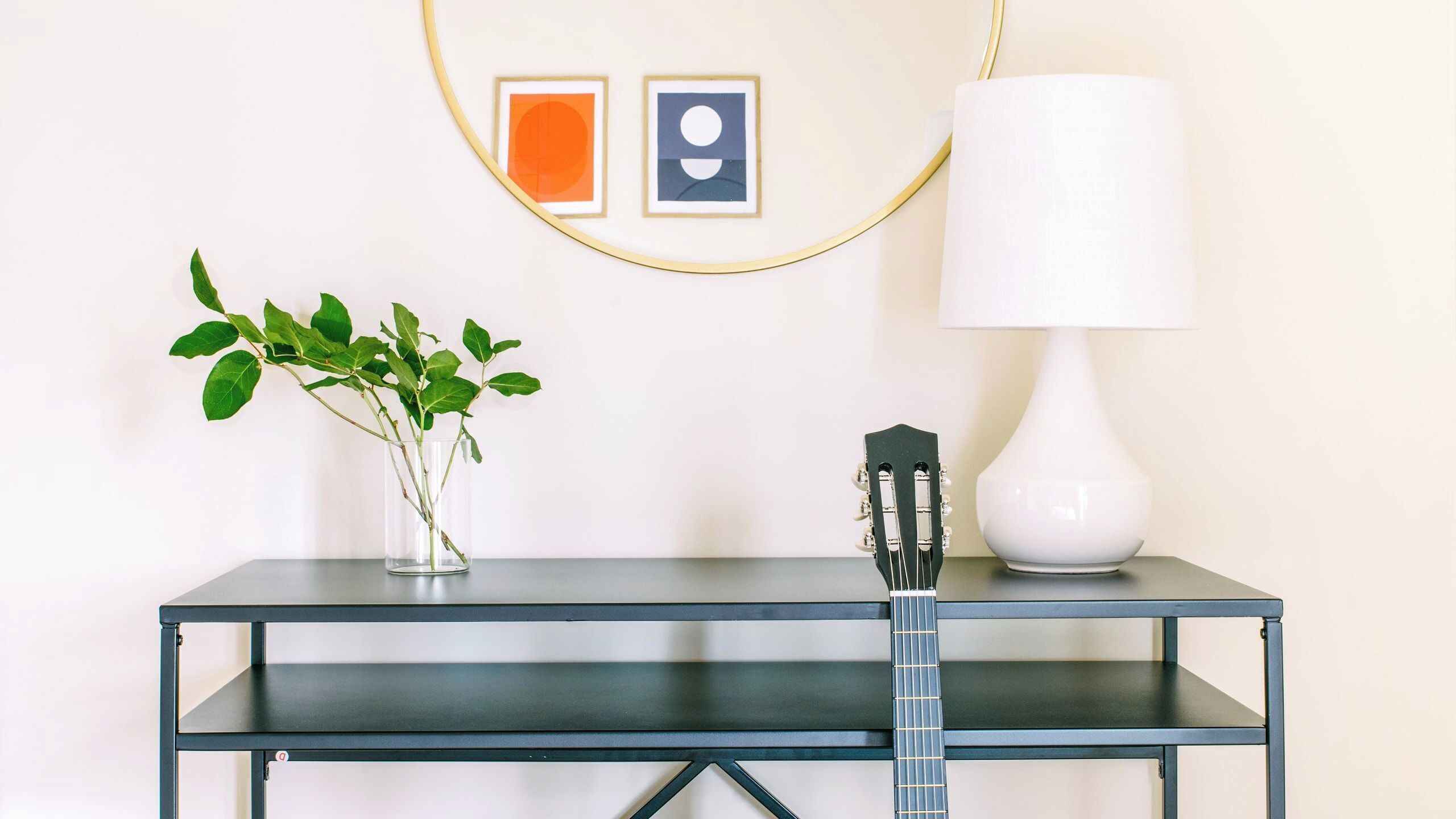 Ett skrivbord med en gitarr, en vas med gröna blad och en lampa.