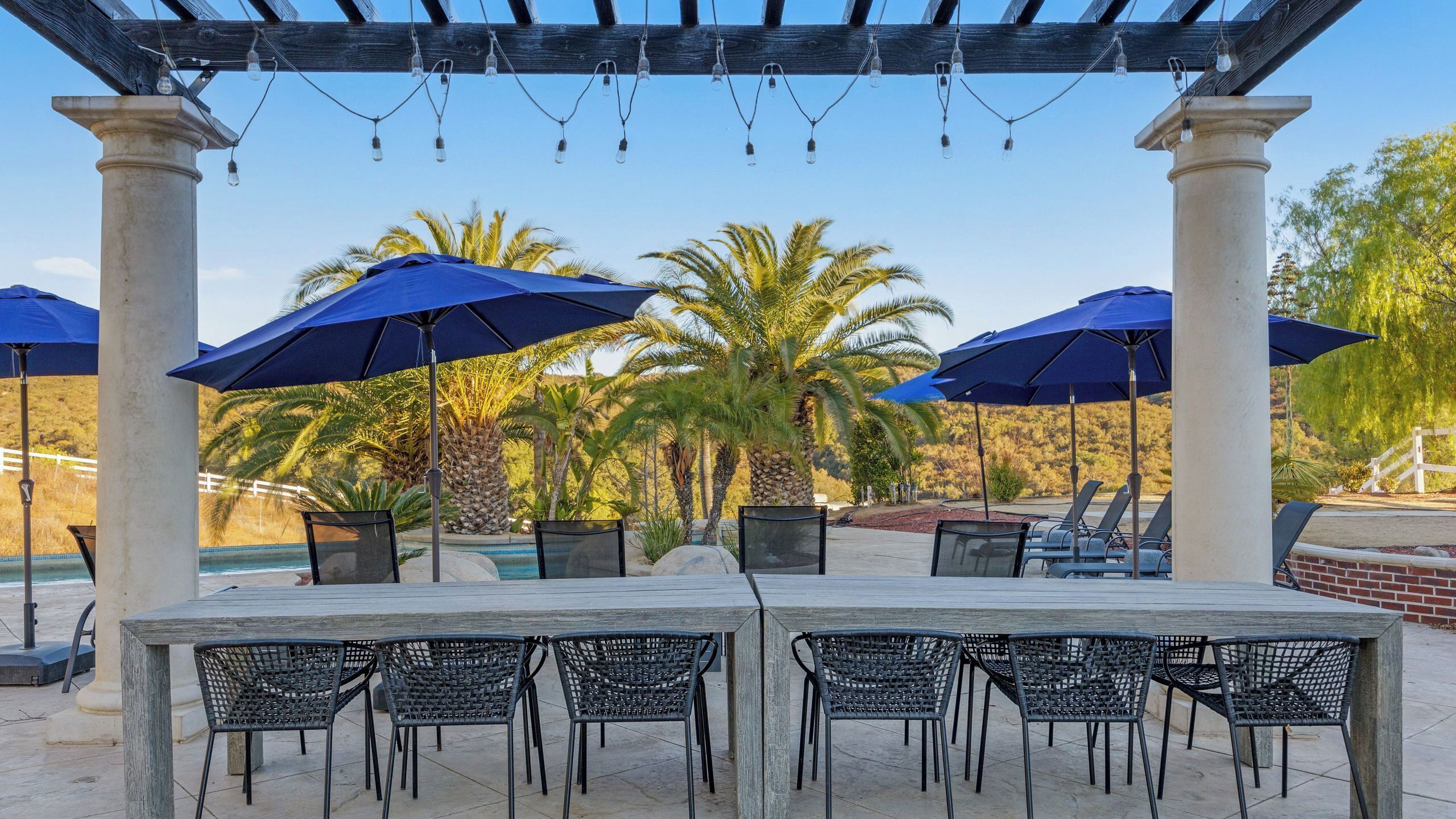 Eine Poolterrasse im Freien, umgeben von Palmen und blauen Sonnenschirmen.