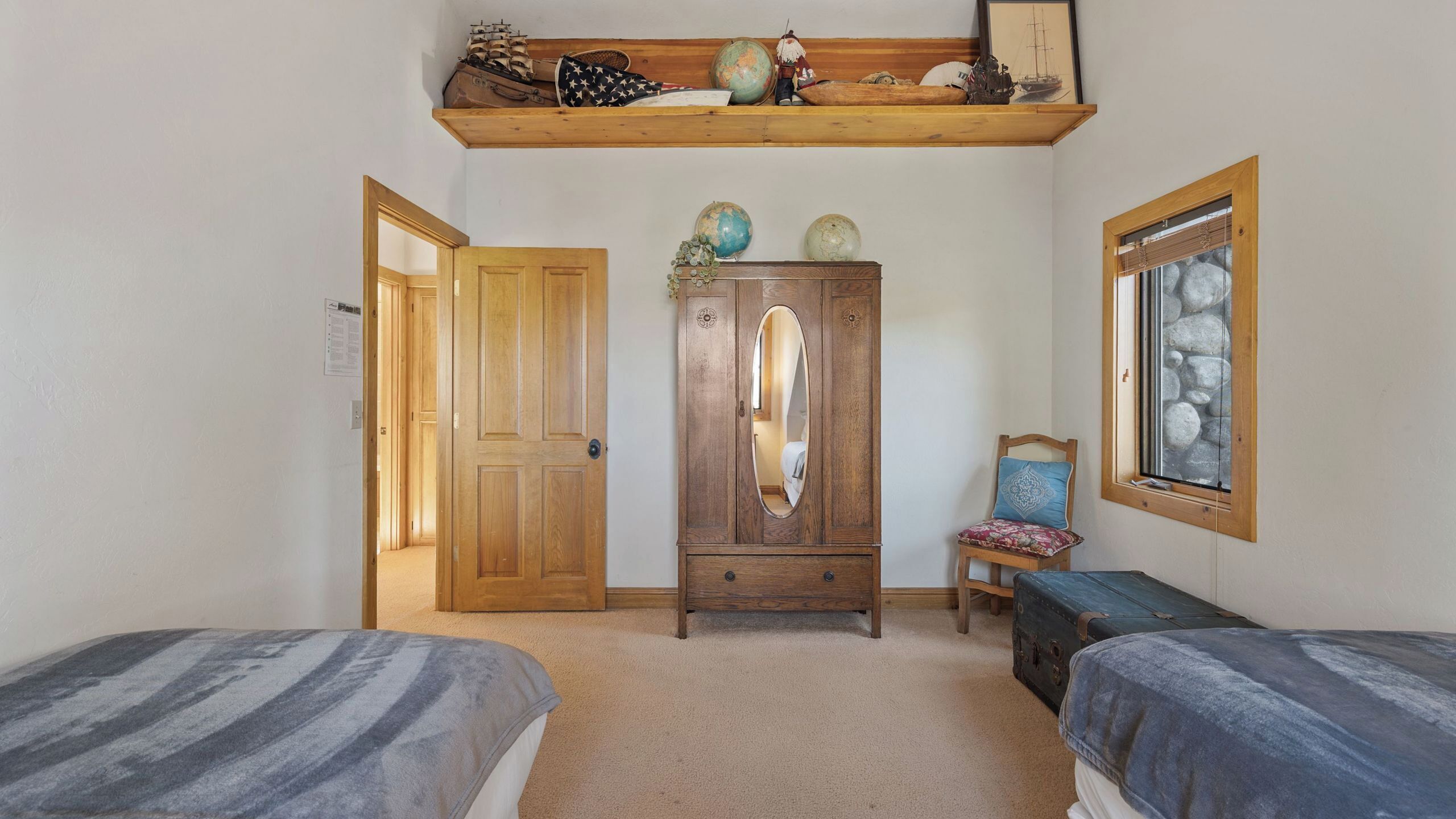 Une pièce avec deux lits, une armoire en bois, une chaise, une fenêtre donnant sur un mur en pierre et une étagère contenant divers objets.