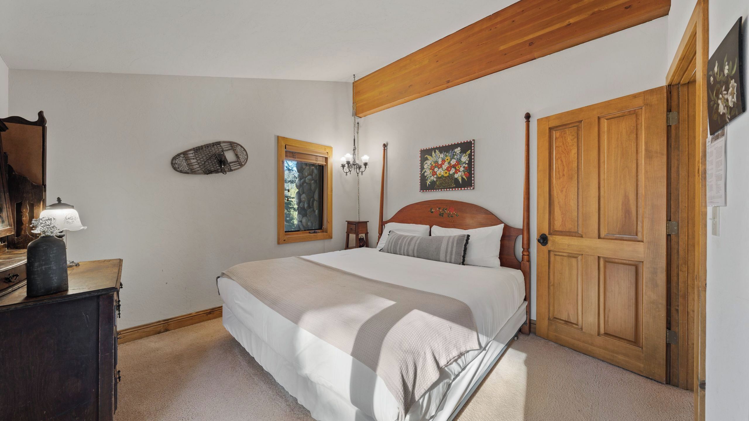 Un dormitorio con cama, una puerta de madera, ventana con vistas, candelabro y decoración en la pared.
