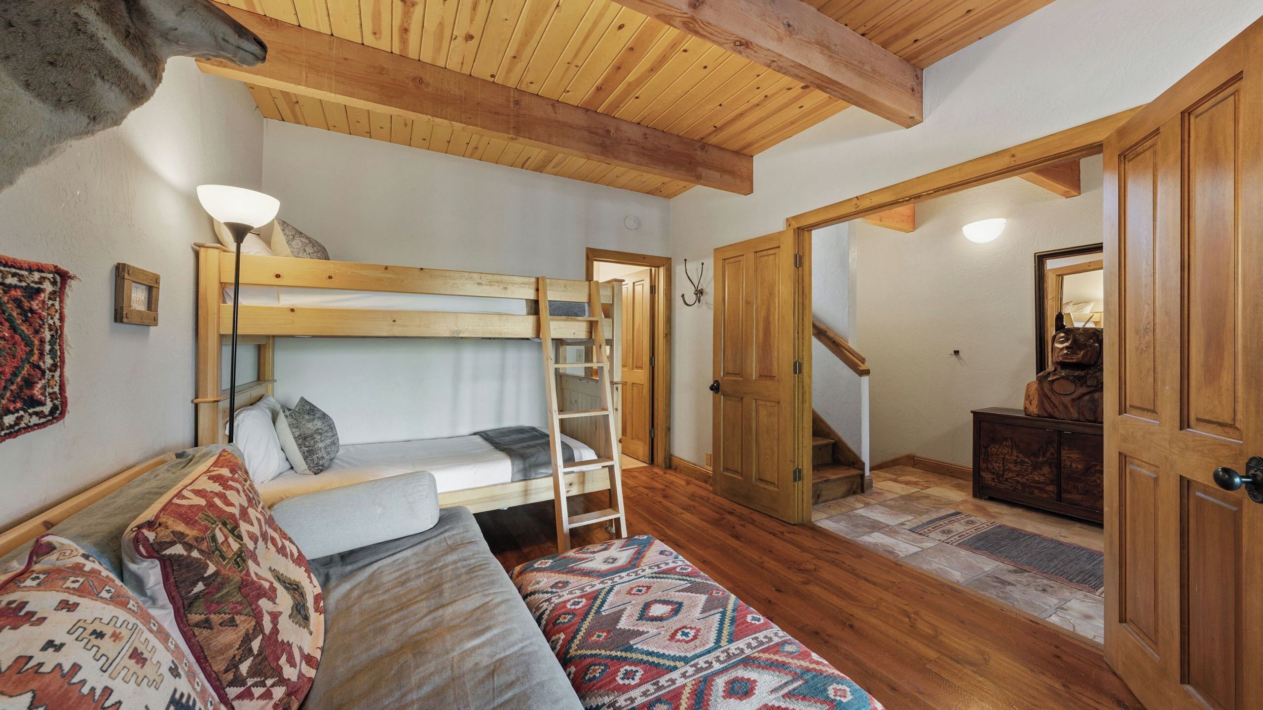 A cozy room with a bunk bed, a wooden ladder, a patterned rug, and a wooden door leading to another room.