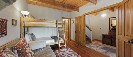 A cozy room with a bunk bed, a wooden ladder, a patterned rug, and a wooden door leading to another room.