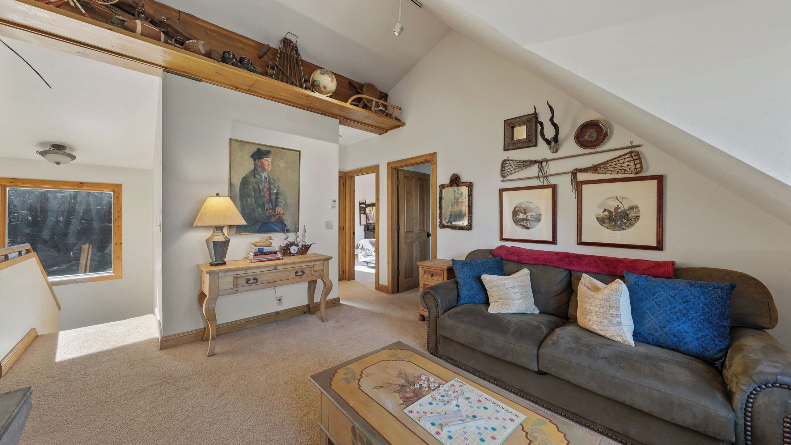 Un salón estilo loft con techo alto, una consola de madera, un sofá con cojines, una mesa de centro con un juego de mesa y obras de arte en las paredes.