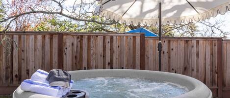 A hot tub with a wooden fence in the background, an umbrella, and a towel and cap on the tub's edge.